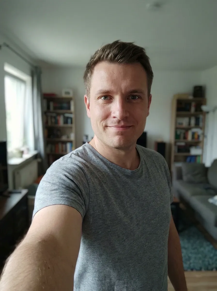 Original selfie input — man in a gray T-shirt at home